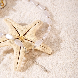 Bohemian seashell and starfish pendant necklace with pearls on white sand background