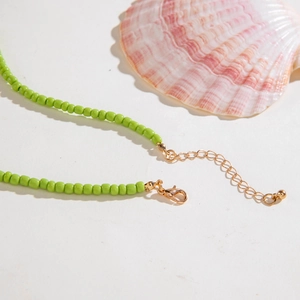 Light green beaded ocean necklace with gold adjustable clasp on a white beach setting