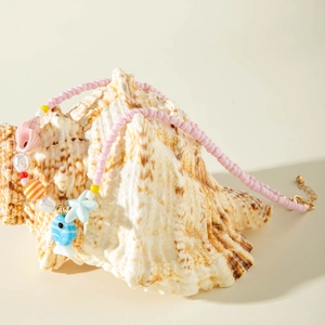 Detail of pink seed bead necklace with starfish, shell, and fish charms on a seashell