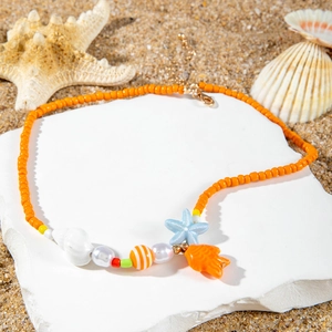 Detail of starfish and shell charms on orange beaded necklace over beach sand backdrop
