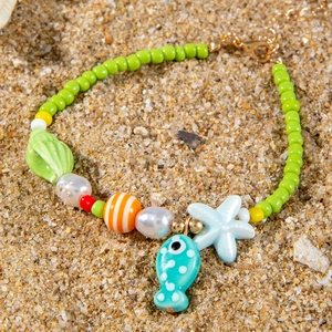 Detail of beach jewelry with starfish and seashell beads on a natural sand background