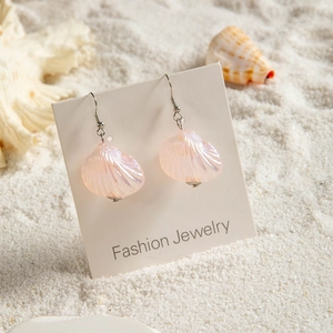 Detail of pink gradient shell earrings with silver hooks on white sand beach background