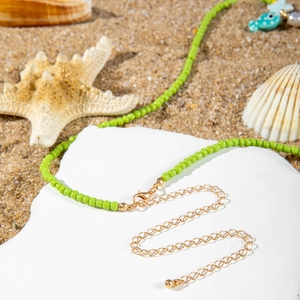 Detail of green beaded summer necklace with starfish and golden lobster clasp on sand