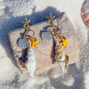 Macro detail of beach style earrings featuring natural conch, starfish, and scallop shells