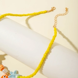 Close-up of beaded necklace with yellow beads and blue star pendant on white stand