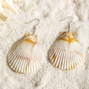 Detailed close-up of natural seashell earrings on white sand beach background