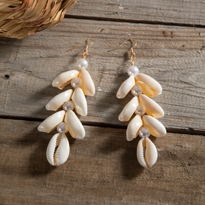 Detail view of long bohemian shell earrings with white pearls on wooden texture