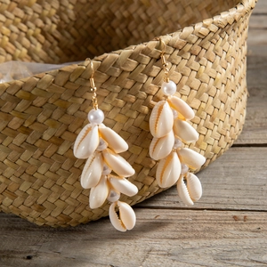 Detail of seashell drop earrings with pearls and gold hooks on a woven texture
