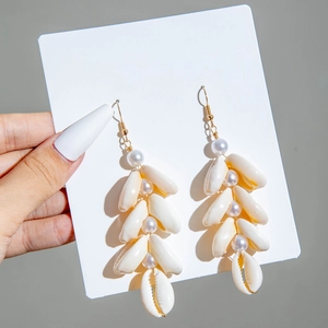 Detail of seashell and pearl drop earrings featuring natural cowrie shells and gold hooks