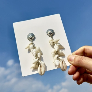 Detail of beach-style seashell dangle earrings with white conch shells against blue sky