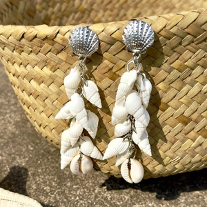 Detail of beach style shell earrings with natural conch hanging on a straw bag