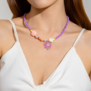 Detail of purple beaded necklace with pink rose and translucent flower pendant charm