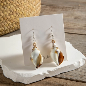 Detail of seashell drop earrings with silver hooks on white stone display