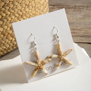 Detailed view of beige starfish drop earrings with natural textures on a white stone board
