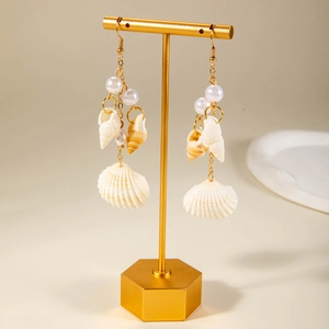 Close-up of beach style shell and pearl earrings on a gold display stand with soft lighting