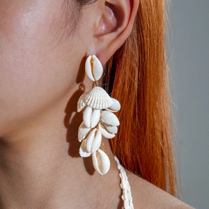 Detail of natural seashell drop earrings featuring white cowrie shells on a female model