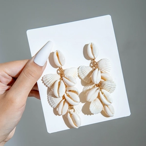 Detail of natural seashell tassel earrings with cowrie and scallop shells on gold hooks