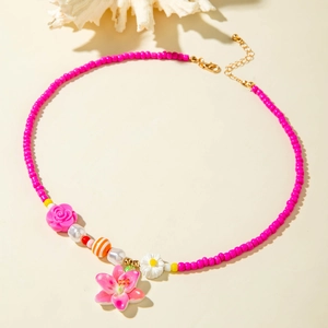 Close-up of vibrant pink beaded necklace with floral charms and white coral background