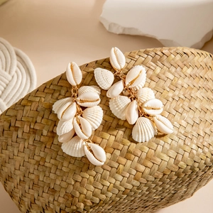 Detail of natural seashell drop earrings with golden chain on a woven straw background