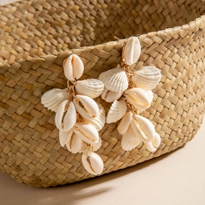 Close-up of tiered natural seashell tassel earrings on a woven straw basket
