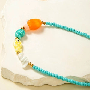 Macro detail of tropical beaded necklace with turquoise shells and yellow fish charms