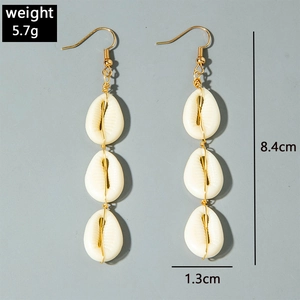 Detail of beach-style long drop earrings with white cowrie shells and gold hooks