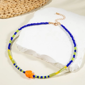 Detail view of colorful beaded necklace with orange fish charm on white stone