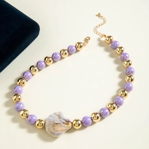 Close-up of beach necklace with purple iridescent beads and a large gold shell pendant
