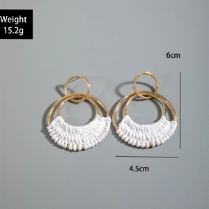Macro detail of geometric raffia earrings with gold rings and white hand-woven rope accents