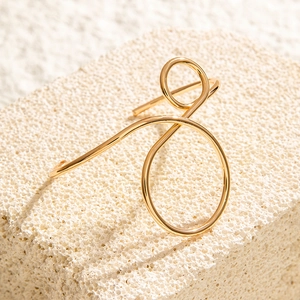 Macro detail of minimalist gold curved ear cuff on textured white stone background