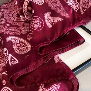 Detailed macro view of deep burgundy paisley silk shawl with smooth satin texture