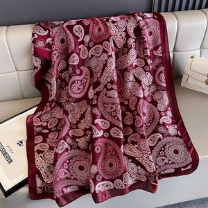 Elegant wine red paisley print satin beach shawl draped on a beige leather sofa with props