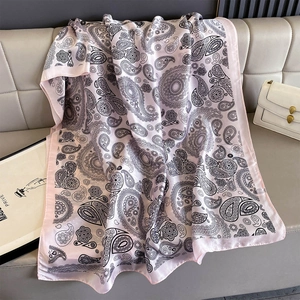 Detail of light pink silk-feel scarf with black paisley print on a gray sofa