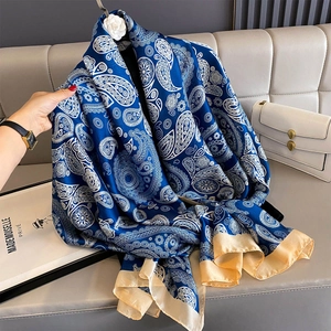 Navy blue paisley beach scarf with gold borders draped over a sofa in a luxury setting