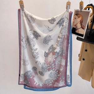 Floral print silk scarf with purple borders hanging next to a beige coat and handbag