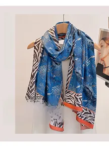 Blauer Strandschal mit Zebra- und Leopardenmuster, orangen Kanten, an einem Holzbügel