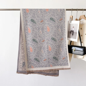 Elegant grey-purple paisley shawl with orange accents and fringes on a metal hanger