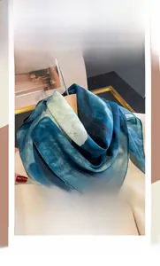 Detail of blue and green tie-dye silk cotton square scarf draped over a wooden hanger