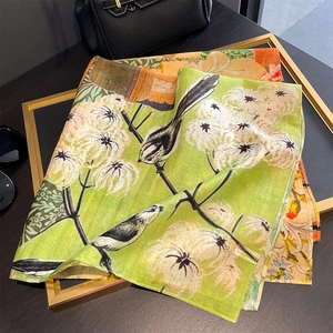 Floral green square scarf with bird print displayed with accessories on a frame