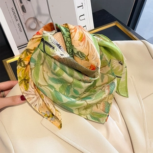 Elegant floral silk scarf with green and orange botanical prints on a beige blazer