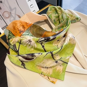 Elegant silk scarf with bird and floral print draped over a beige blazer on hanger
