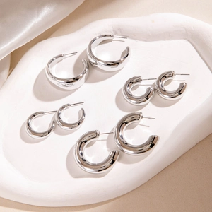 Set of four minimalist silver C-shaped hoop earrings in various sizes on a textured tray