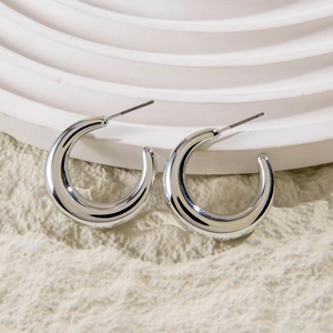 Detailed view of polished silver C-shaped hoop earrings on minimalist geometric props