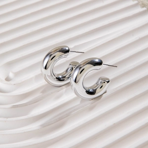 Detail view of silver C-shaped chunky earrings with polished finish on a white tray