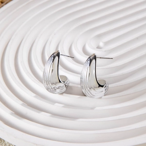 Macro detail of silver crescent earrings with textured vertical ridges and glossy finish