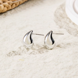 Close-up of polished silver teardrop earrings with shiny metallic finish on textured surface