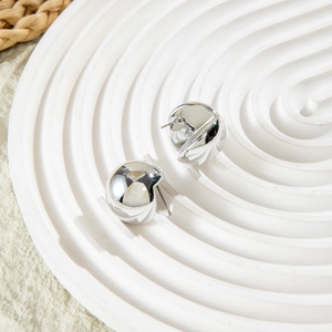 Macro detail of silver geometric earrings with a polished hammered texture on white tray