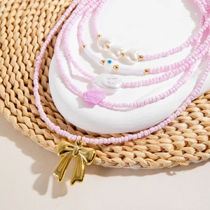 Detail of layered pink beaded necklace with golden bow pendant and floral charms