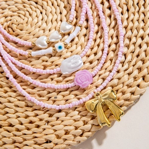 Pink beaded necklace with golden bow pendant and blue evil eye charms on straw mat