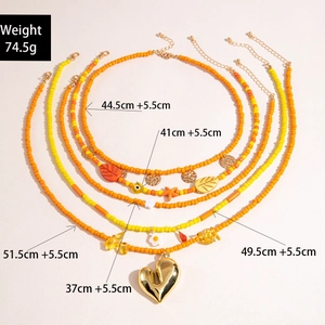 Detail view of 5-piece layered beaded necklaces with orange beads and gold heart charms